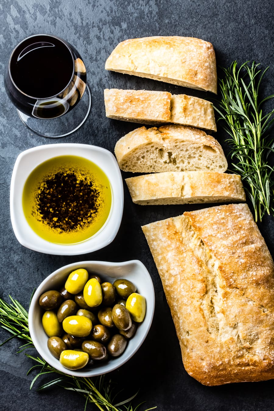Ciabatta, pepper oil, olives, arugula, rosemary, slate background