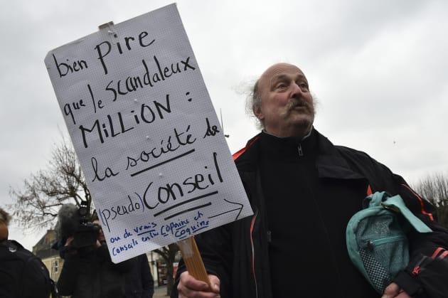 A man holds a placard reading "Much worse than the scandalous Million, the consulting company" during a gathering of demonstrators who came to express their discouragement, after the revelations by The "Canard Enchaine" of the supposedly fictional jobs of Penelope Fillon on February 11, 2017, in Sable-sur-Sarthe, northwestern France. Winner of the right-wing primaries ahead of France's 2017 presidential elections, Franï¿½ois Fillon was elected mayor, councillor general, deputy, in Sable-Sur-Sarthe, after the death of Joel Le Theule. / AFP PHOTO / JEAN-FRANCOIS MONIER