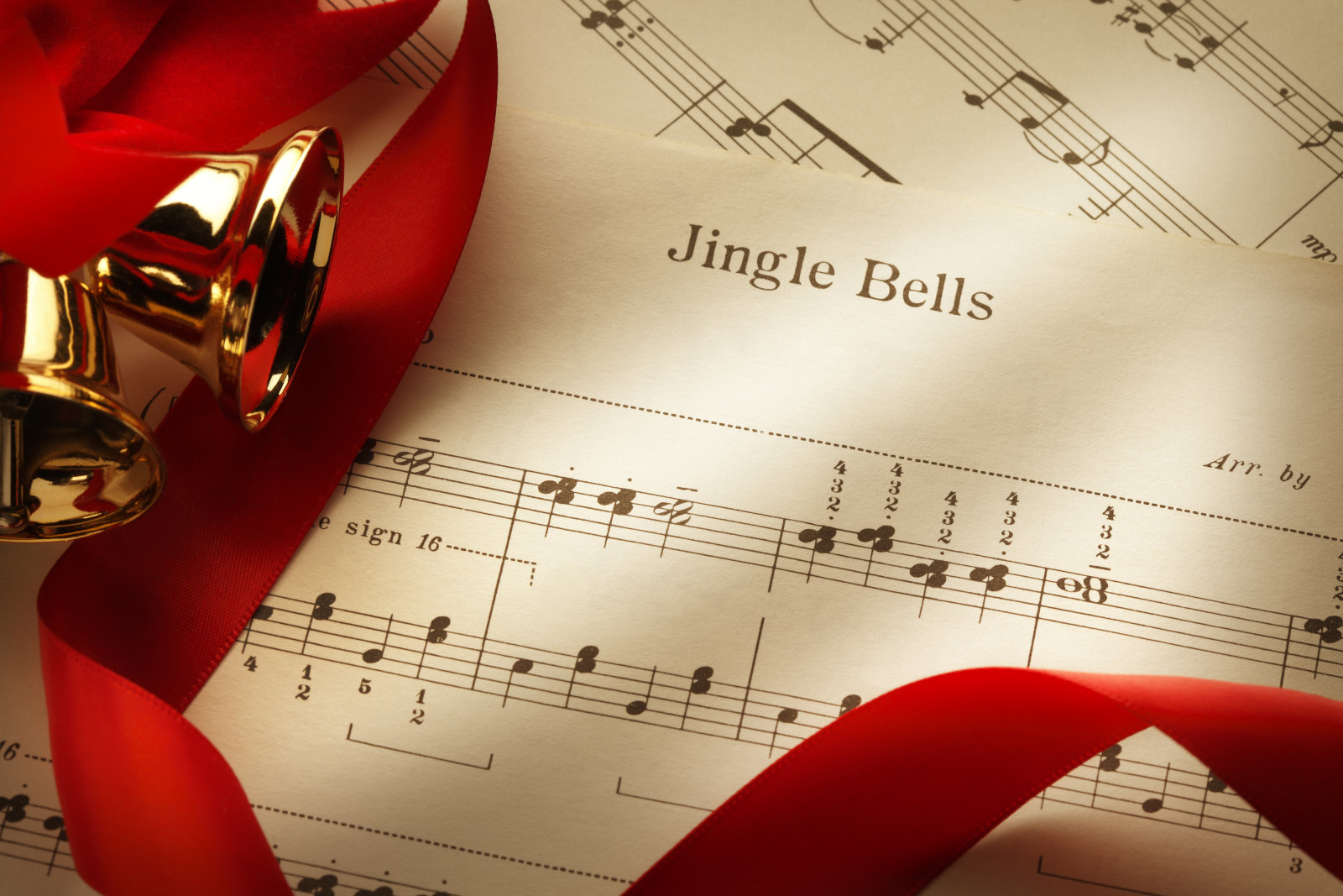 Several Christmas bells and red ribbon on the sheet music from the Christmas classic, Jingle Bells.
