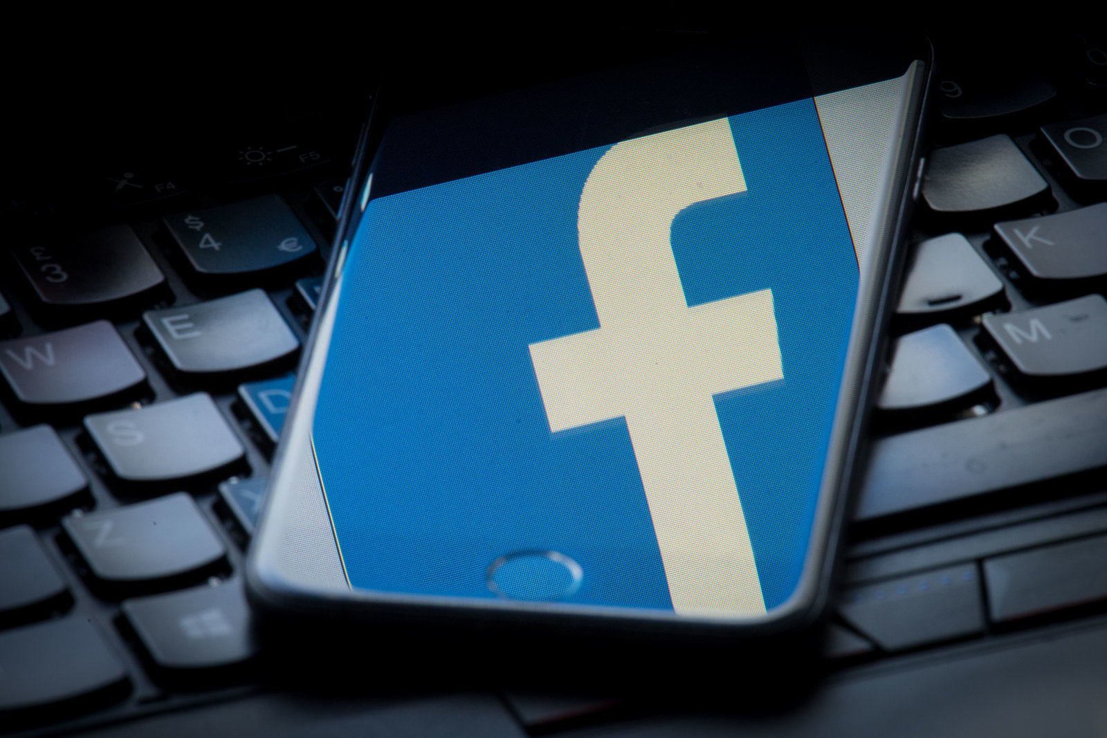 The logo of social networking site Facebook is reflected on the screen of a smartphone resting on a laptop keyboard. (Photo by Dominic Lipinski/PA Images via Getty Images)