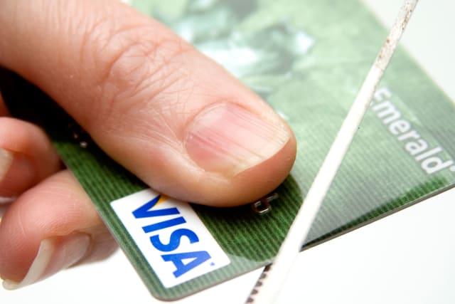 Concept of hand holding a visa credit card while scissors cuts it up symbolizing lean times