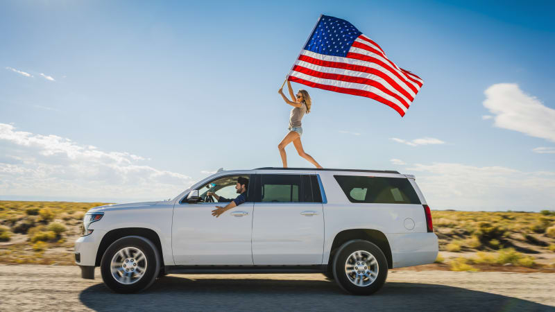 hispanic-woman-waving-american-flag-on-roof-of-white-suv-picture-id672153421