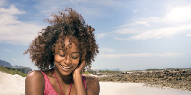 A photo of sensuous young woman at beach. Smiling attractive female is enjoying wind during vacation. She is wearing tank top.