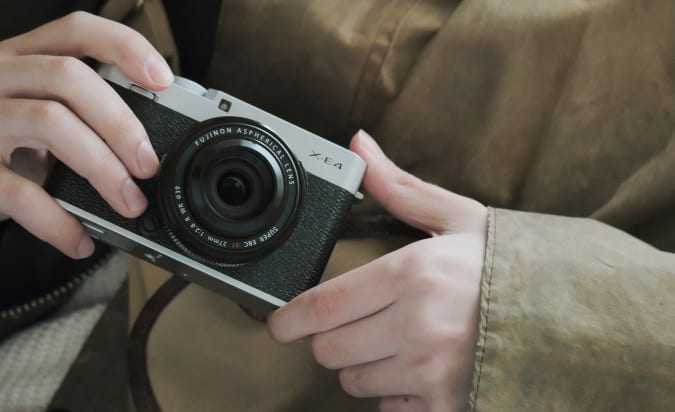 A Fujifilm X-E4 held in someone's hands close to their chest.