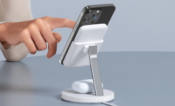 A person touching the screen of an iPhone that's propped up on Anker's 633 MagGo 2-in-1 Wireless Charging Station.