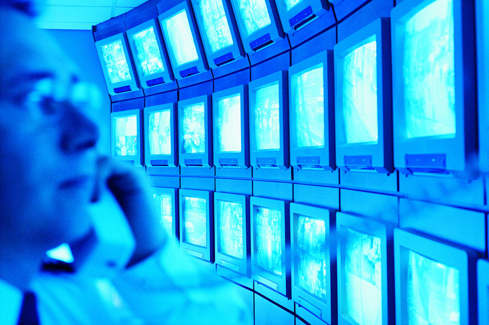 Man in a Control Room Using a Telephone and Looking at a Large Group of Surveillance TV Screens