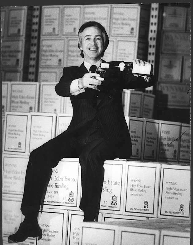 South Australian Premier Don Dunstan sitting on wine boxes from Wynn's High Eden Estate pouring a glass of wine in July 1978.