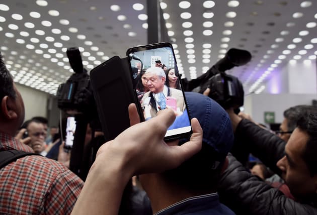 Un pasajero toma una fotografía del presidente mexicano López Obrador, asediado por la prensa antes de...