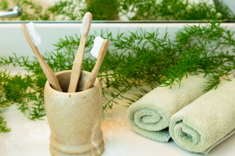 Bamboo toothbrushes in cup, towels and greens on bathroom countertop
