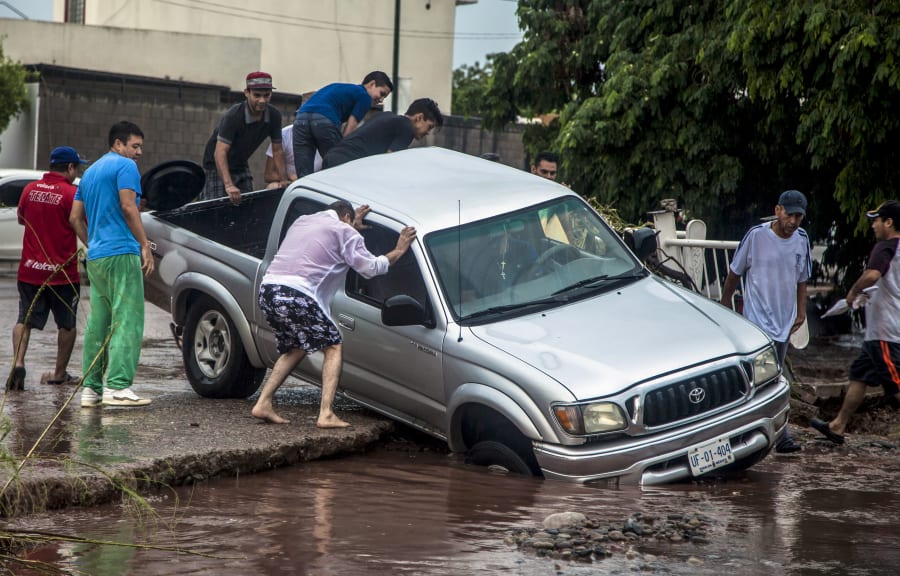 La gente intenta rescatar una camioneta antes de que caiga a un socavón generado tras las intensas lluvias.