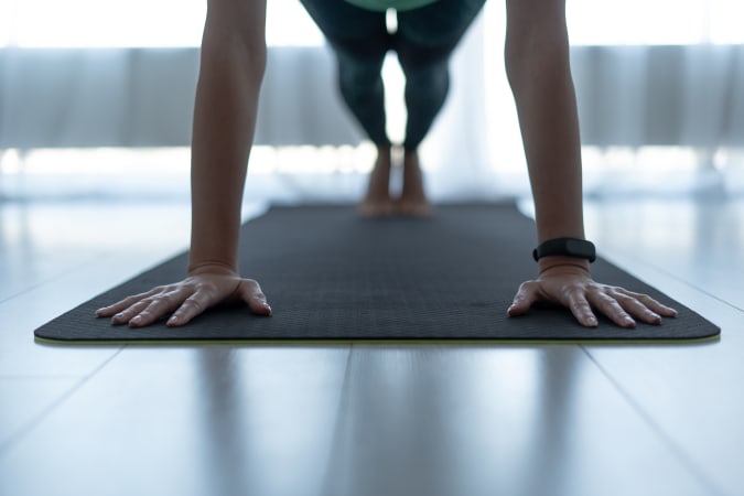 Cropped view of sporty and young adult woman standing in plank pose on fitness mat at home