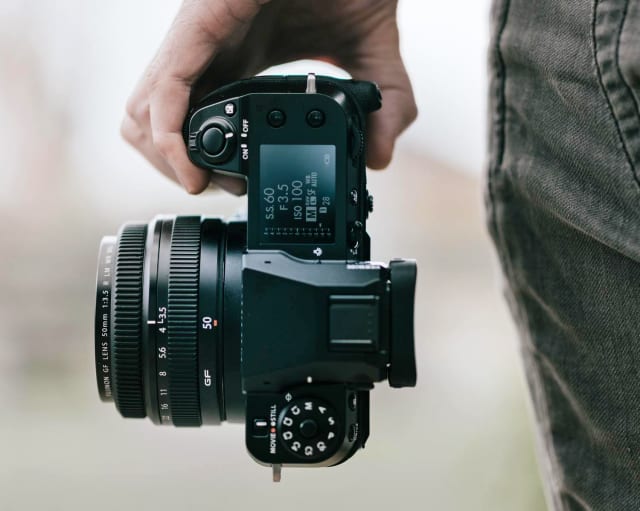 Fujifilm's GFX 100S has a massive 102-megapixel sensor and a compact body.  He is shown here held next to someone by his leg, cut off just to the camera and the leg.