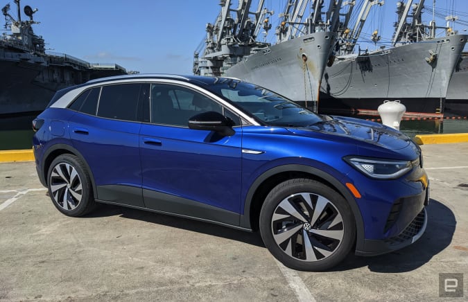 A blue Volkswagen ID.4 EV is parked in a lot right next to San Francisco docks with military ships.