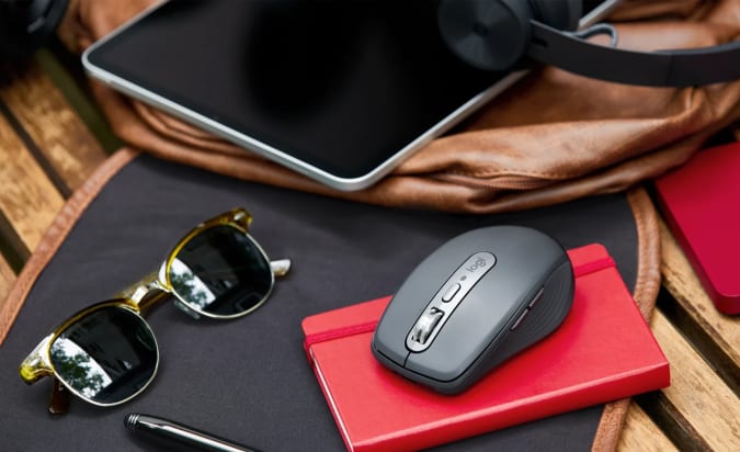 The Logitech MX Anywhere 3 sits on a laptop next to sunglasses and a tablet.