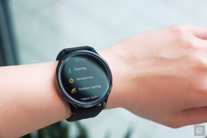 OnePlus Watch review photos. OnePlus Watch on a wrist showing a list of workouts including Running, Fat Burn Run, Outdoor cycling and Indoor cycling.