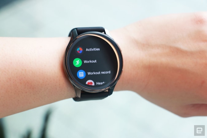OnePlus Watch review photos. OnePlus Watch on a wrist with display showing a list of apps including Activities, Workout, Workout record and Heart...