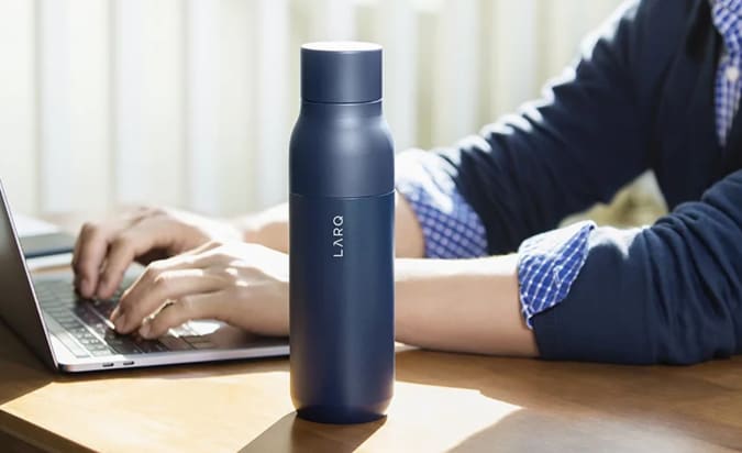 A LARQ Bottle PureVis on a desk next to someone working on a laptop.