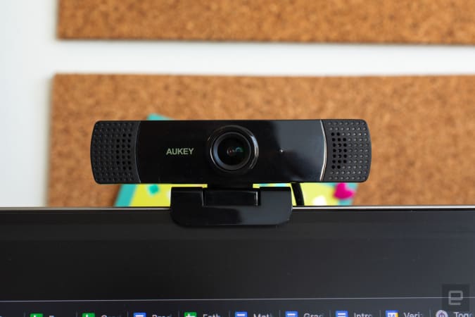 Aukey FHD webcam clipped to a computer monitor with a cork board in the background.