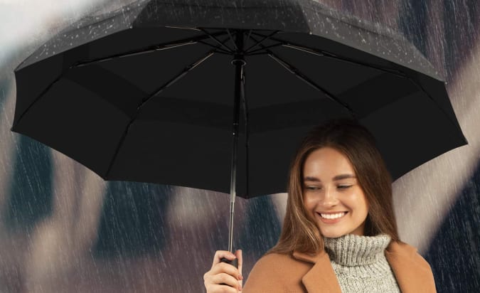 A woman in the rain huddled under a Repel travel umbrella.