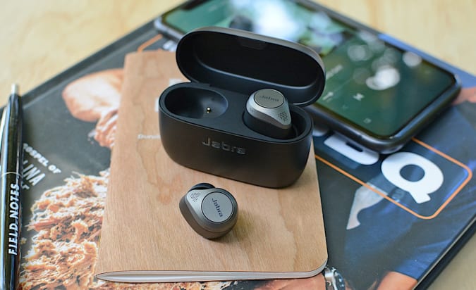 The Jabra Elite 85t and charging case sitting on top of magazines on a countertop.