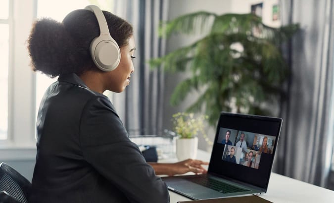 A woman wearing a light colored pair of Sony WH-1000XM4 headphones while on a video call.