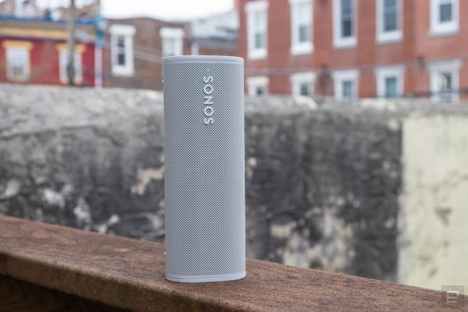 Sonos Roam portable speaker outside, standing vertically on a wooden railing.