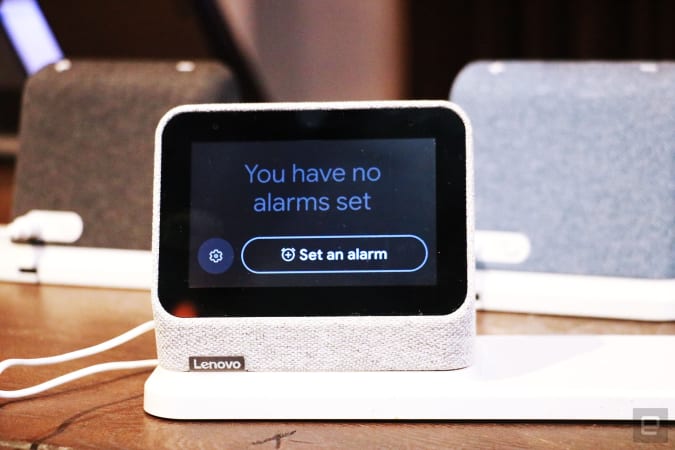 A gray Lenovo Smart Clock 2 on a wireless charging dock with its screen facing the camera. The display shows the Alarm page, with the words 
