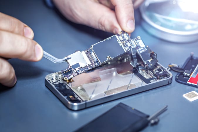 Technician repairs the damaged mobile phone. Serviceman is repairing a damaged cell phone. Technician repairs the damaged smartphone. Replacing the smartphone's motherboard.
