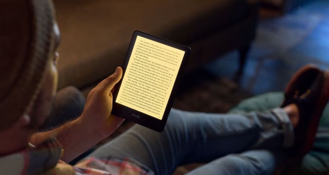 A person sitting reading a text on a fifth generation Kindle Paperwhite.