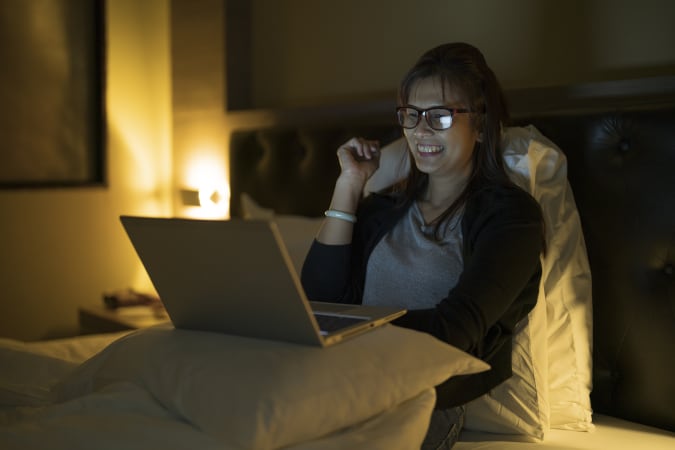 Young woman watching tv on her laptop in bed at night.
