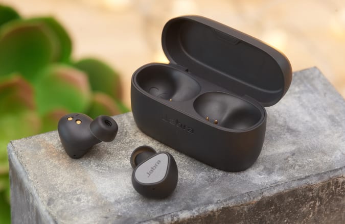 Jabra Elite 3 earbuds and case in black on a concrete block with a plant in the background.