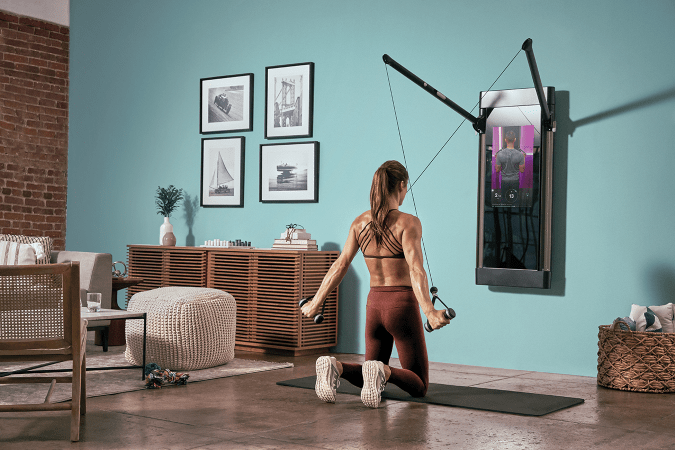 A woman, using a tonal wall-mounted workout system, pulls down. 