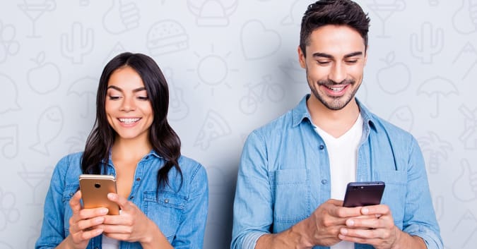 Stock image of a woman and man standing next to each other on their smartphones.