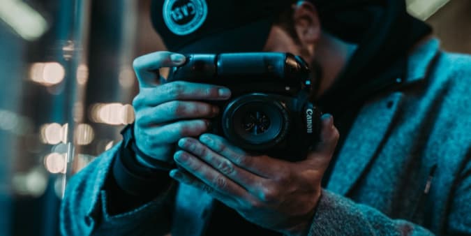 Stock image of a man in a baseball hat using a Canon DSLR camera.
