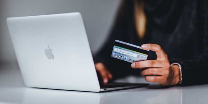 Stock image of a woman sitting in front of a MacBook with a credit card in hand.