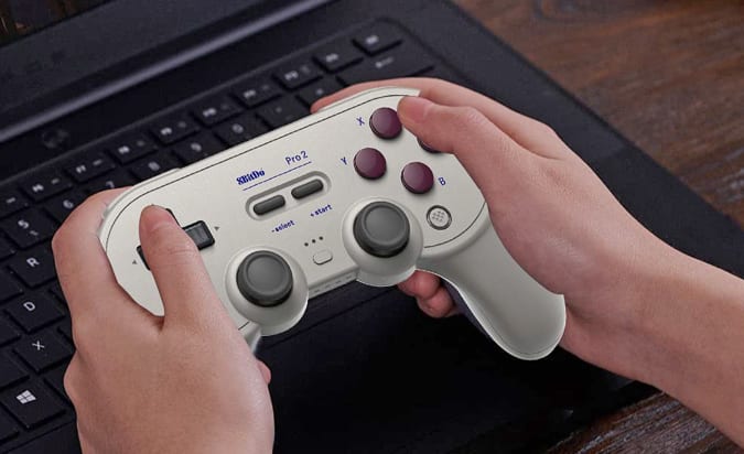 Hands holding the 8BitDo Pro 2 controller above a laptop keyboard.