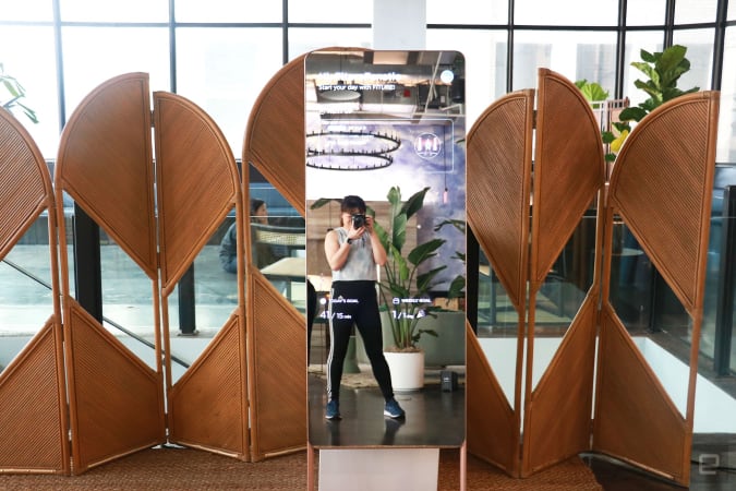An interactive exercise mirror from Fiture shows a summary page, with a woman holding a camera in reflection.