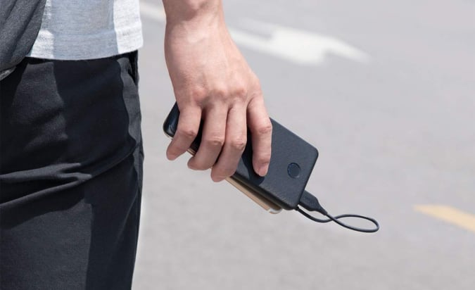 A hand holding a mobile phone connected via a cable to the Anker PowerCore Slim 10K portable power bank.