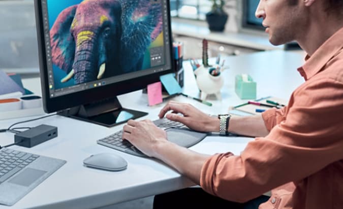 Um homem sentado em uma mesa em frente a um computador com as mãos no teclado ergonômico Microsoft Surface.