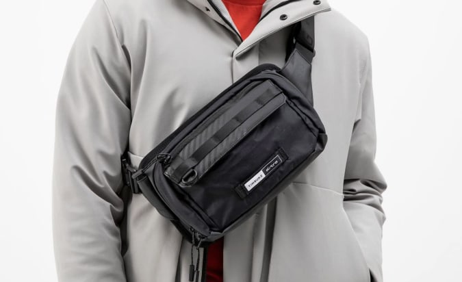 A man wearing a gray jacket with the Timbuk2 Crossbody sling across the chest.