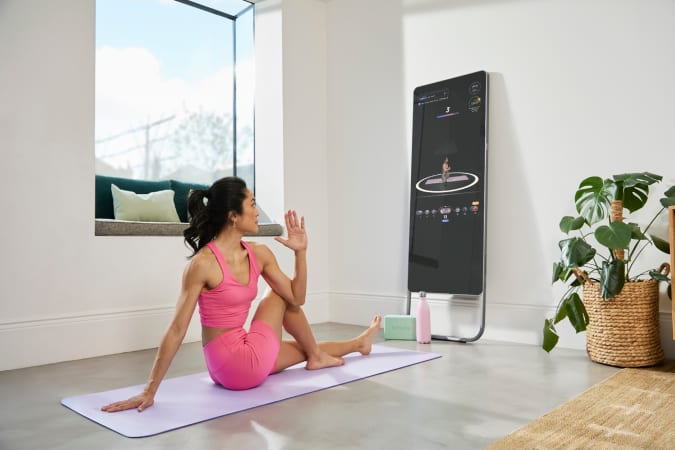 O persoană care stă în fața unei oglinzi interactive de antrenament Fiture pe un covoraș de yoga, efectuând o răsucire a coloanei vertebrale. 