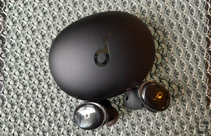 Black wireless earbuds and their charging case on a chain metal background.