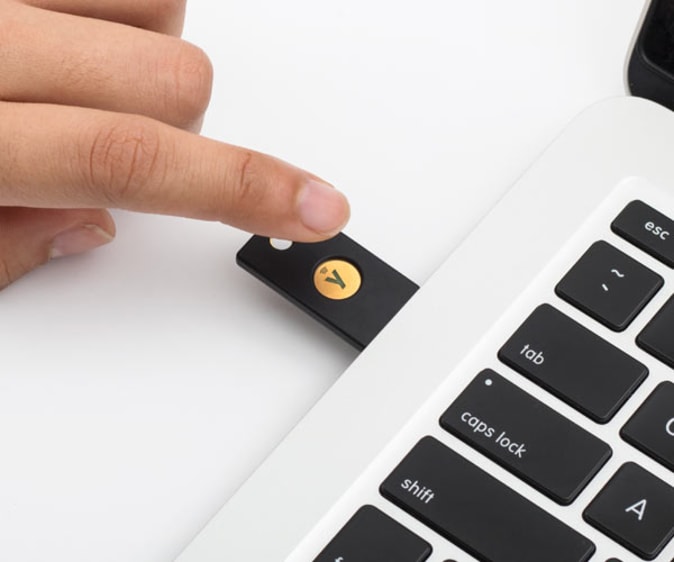 Yubico YubiKey NFC 5 security key in the laptop port with a human finger that reaches out to touch it.