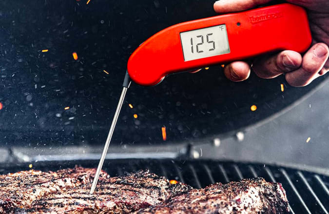 The ThermoWorks Thermapen One thermometer checking the temperature of a piece of meat cooking on a grill.