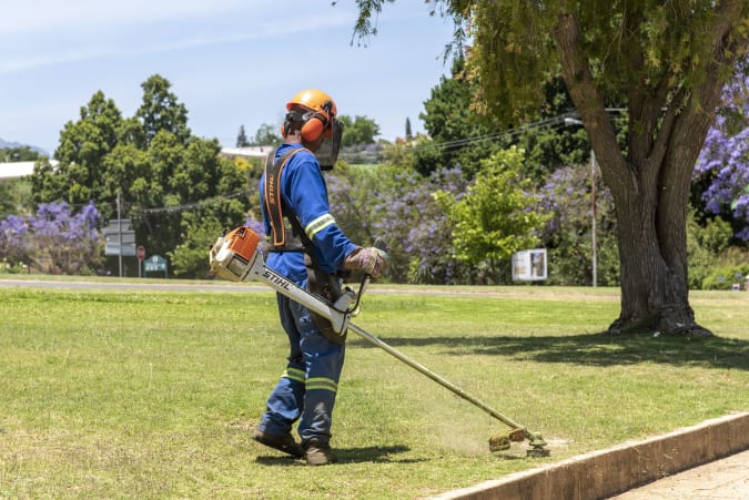 Western Cape, South Africa, Man wearing protective clothing and safety helmet trimming grass in a garden. (Photo by: Peter Titmuss/Education Images/Universal Images Group via Getty Images)