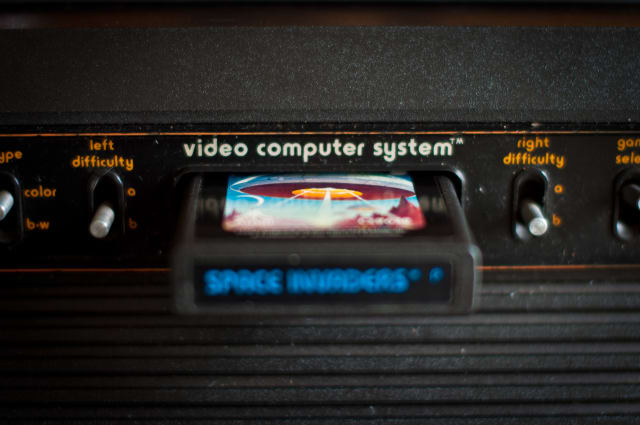 [UNVERIFIED CONTENT] Atari 2600 VCS console, close up of inserted cartridge and central switches. Space Invaders game is inserted. Difficulty switches visible. Narrow depth of field. Dust visible.