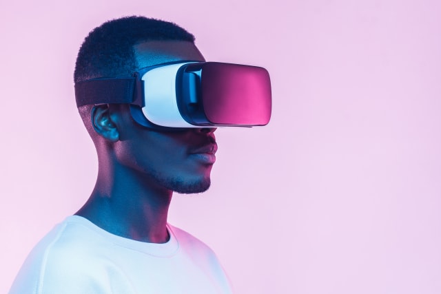 VR concept. Young african man wearing virtual reality goggles, isolated on pink background