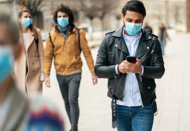 Portrait of young man on the street wearing face protective mask to prevent Coronavirus and anti-smog and using smartphone