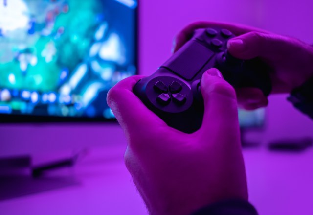 Closeup hands of anonymous male holding modern controller while playing video game in dark room