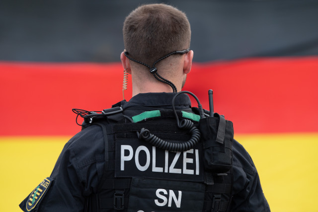 15 June 2020, Saxony, Dresden: A policeman is standing in front of a German flag on the occasion of a rally of the anti-Islamic and xenophobic Pegida-movement on the Altmarkt. Photo: Sebastian Kahnert/dpa-Zentralbild/dpa (Photo by Sebastian Kahnert/picture alliance via Getty Images)